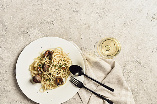 top view of delicious pasta with seafood served with white wine and cutlery on textured grey surface with copy space