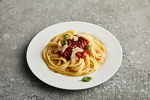 tasty bolognese pasta with tomato sauce and Parmesan on white plate on grey background