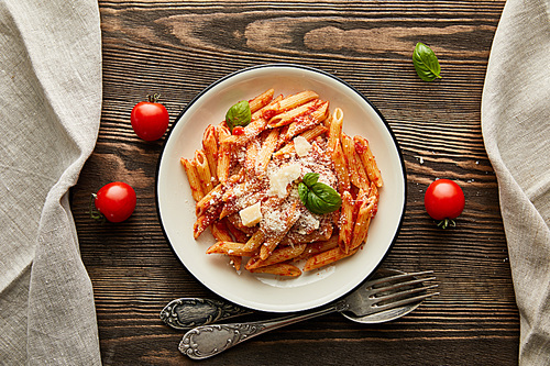 top view of tasty bolognese pasta with tomato sauce and Parmesan in white plate near ingredients and cutlery on wooden table