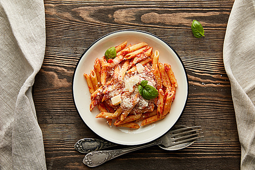 top view of tasty bolognese pasta with tomato sauce and Parmesan in white plate near cutlery on wooden background
