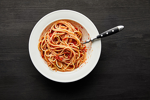top view of tasty bolognese pasta with tomato sauce in white plate on black wooden background