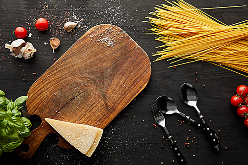 top view of bolognese pasta ingredients, cutting board and cutlery on black wooden background