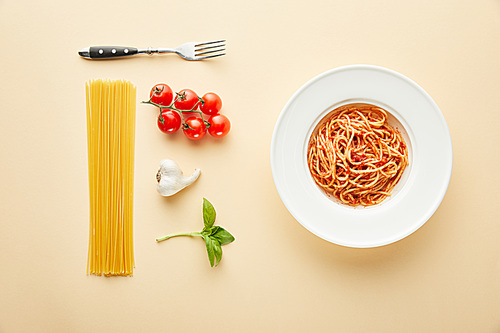 flat lay with delicious spaghetti with tomato sauce in plate near fork and ingredients on yellow background