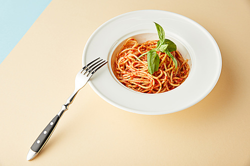 spaghetti with tomato sauce in plate near fork on blue and yellow background