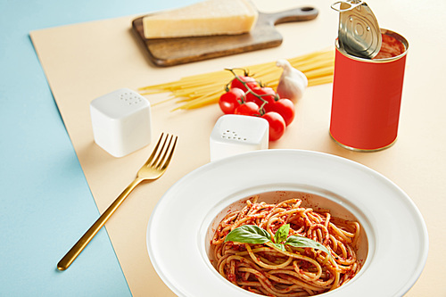 selective focus of delicious spaghetti with tomato sauce in plate near fork on blue and yellow background