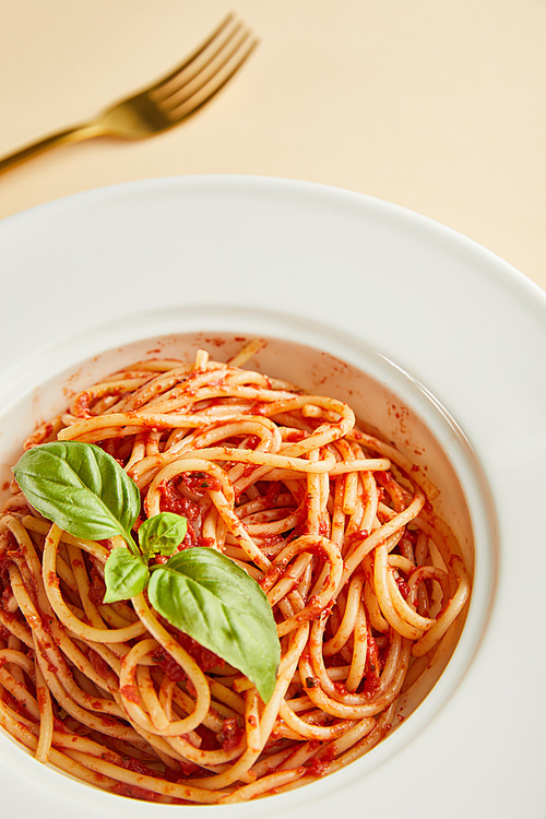 selective focus of delicious spaghetti with tomato sauce and basil in plate near fork on yellow background