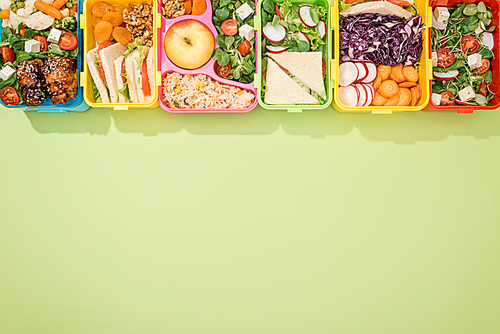 top view of lunch boxes with food on green background
