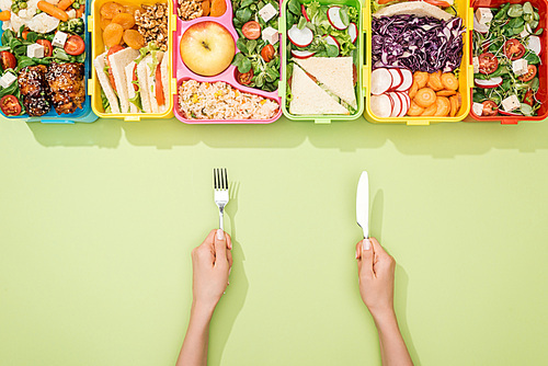 cropped view of woman holding fork and knife near lunch boxes with food