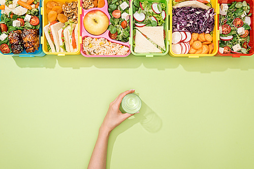 cropped view of woman holding glass of water in hand near lunch boxes with food