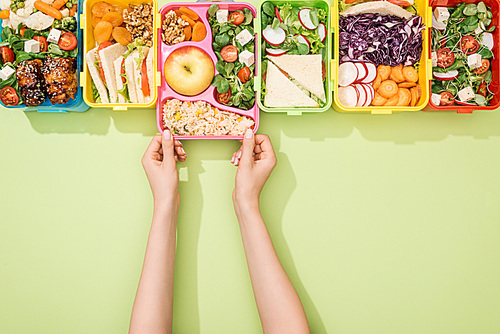 cropped view of woman choosing lunch boxes with food on green background