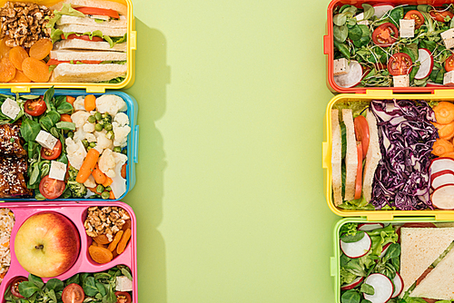 top view of lunch boxes with food on green background with copy space