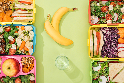 top view of lunch boxes with food near glass of water and bananas