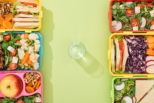 top view of lunch boxes with food near glass of water