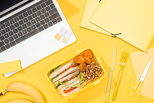 top view of lunch box with food near laptop and office supplies