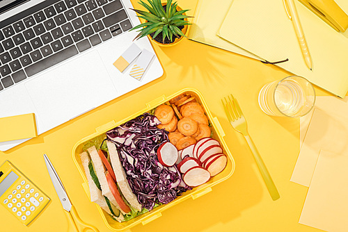 top view of delicious lunch in box at workplace with yellow background