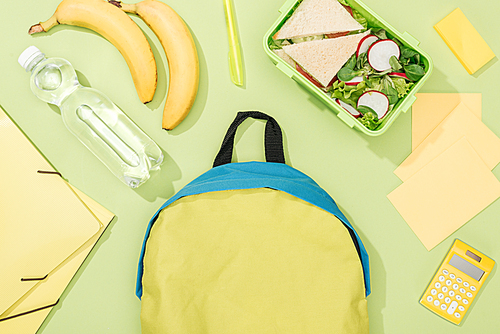top view of lunch box with food near backpack, bottle of water and stationery
