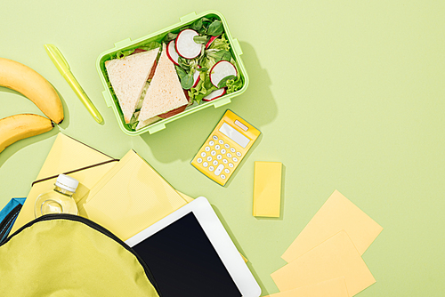top view of lunch box with sandwiches and salad near backpack with stationery