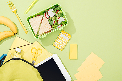 top view of lunch box with sandwiches and salad near backpack with stationery