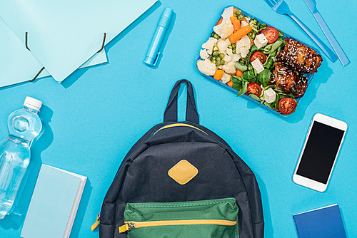top view of backpack near lunch box, stationery, smartphone and bottle of water