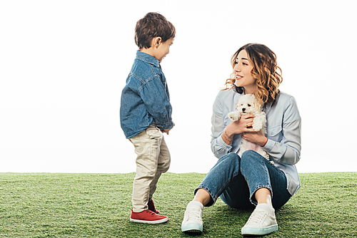 smiling mother holding Havanese puppy and looking at son isolated on white