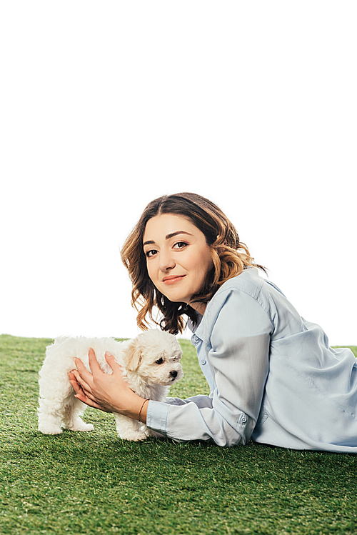 smiling woman holding Havanese puppy and lying on grass isolated on white