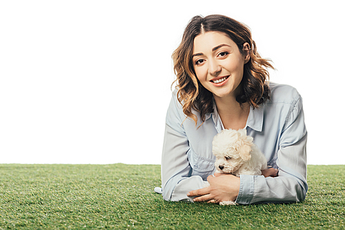 smiling woman holding Havanese puppy and lying on grass isolated on white