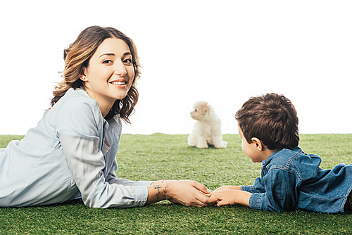 selective focus of smiling mother and son lying on grass and Havanese puppy on background isolated on white