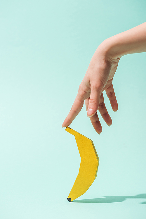 cropped view of young woman touching paper banana on turquoise with copy space