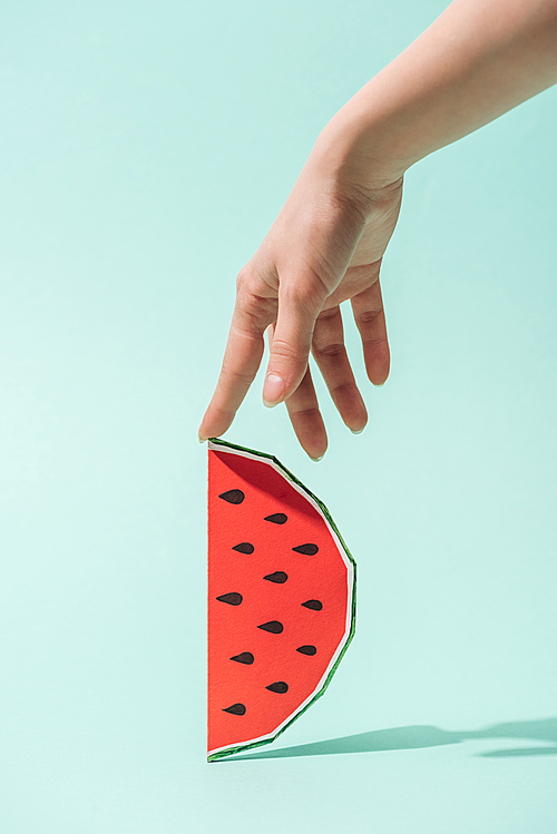cropped view of young woman touching paper watermelon with seeds on turquoise