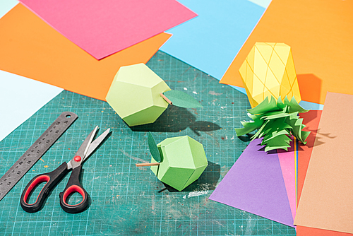 origami fruits and colorful cardboard with scissors and ruler on messy surface