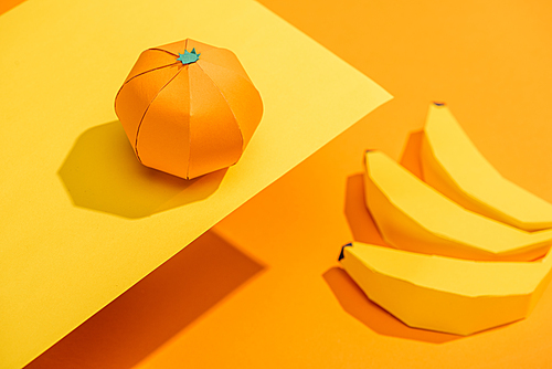 Selective Focus of origami tangerine on yellow paper with cardboard bananas on orange