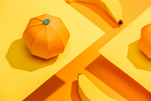 Selective Focus of paper tangerine on cardboard with origami bananas on orange