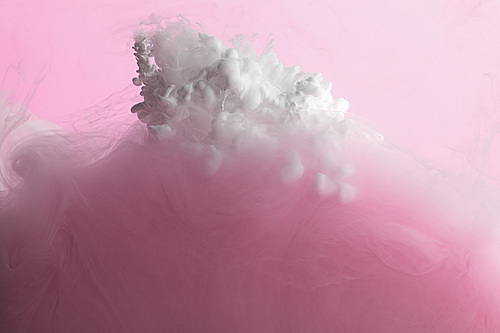 Close up view of white and pink paint mixing in water isolated on pink