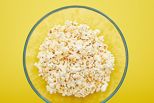 top view of delicious popcorn in glass bowl on yellow background