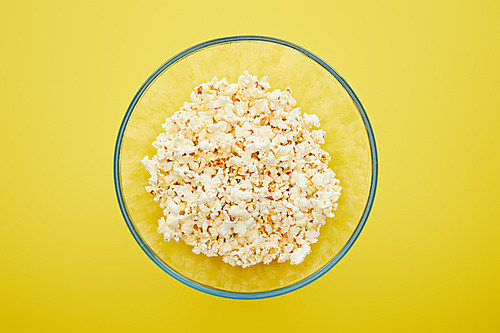 top view of delicious fresh popcorn in glass bowl on yellow background