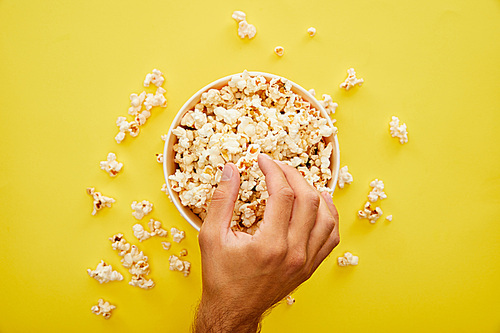 partial view of man taking delicious fresh popcorn from bucket on yellow background