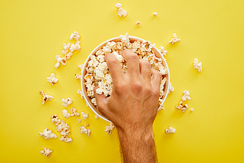 cropped view of man grabbing delicious popcorn from bucket on yellow background