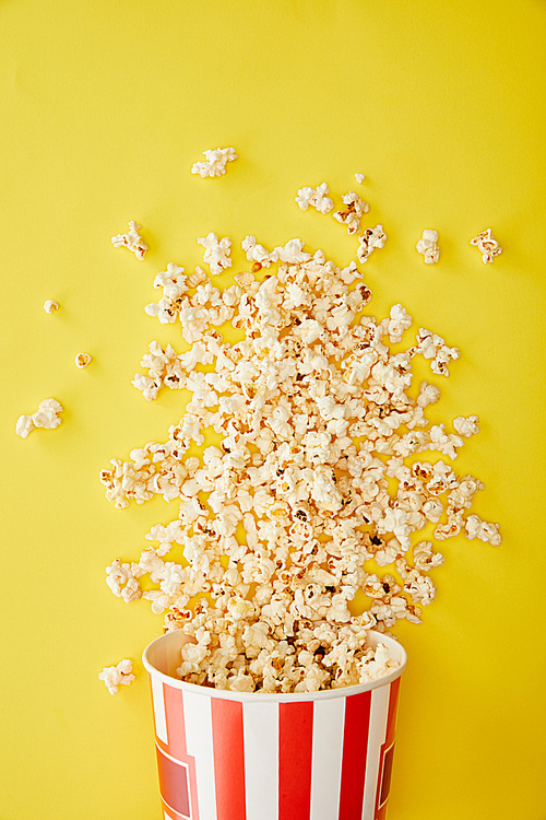 top view of delicious popcorn scattered from bucket on yellow background