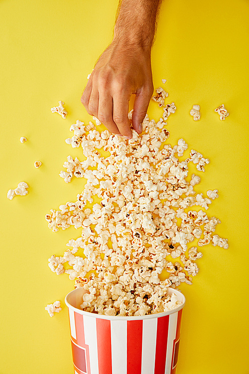 cropped view of man taking delicious popcorn from bucket on yellow background