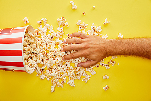 cropped view of man putting hand on delicious popcorn on yellow background