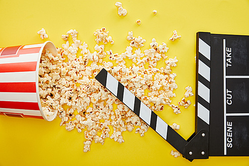 top view of delicious popcorn scattered on yellow background with clapper board