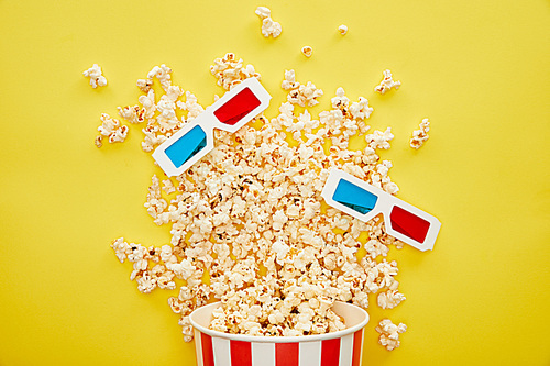 top view of delicious popcorn scattered from bucket and 3d glasses on yellow background