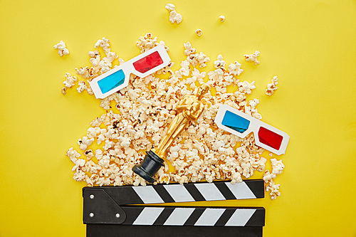 KYIV, UKRAINE - AUGUST 13, 2019: top view of delicious popcorn, 3d glasses and clapper board with golden Oscar statuette on yellow background
