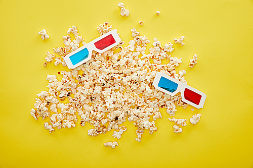 top view of delicious popcorn scattered near 3d glasses on yellow background