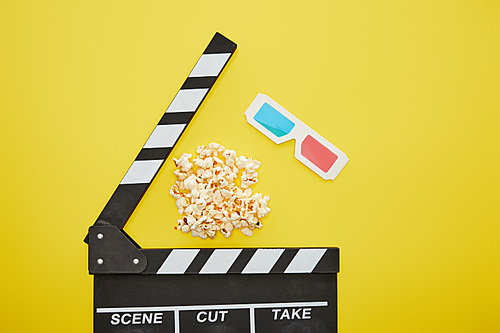 top view of crunchy popcorn near clapper board and 3d glasses on yellow background