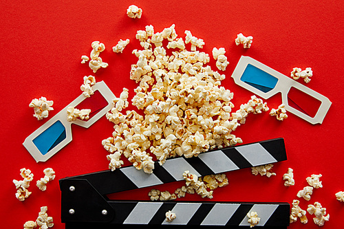 top view of delicious popcorn near clapper board and 3d glasses on red background
