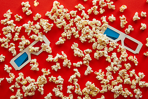 top view of 3d glasses on delicious scattered popcorn on red background