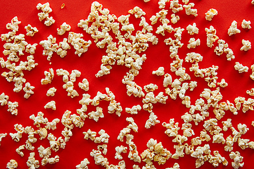 top view of fresh popcorn scattered on red background