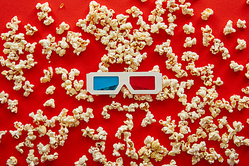 top view of 3d glasses on scattered popcorn on red background