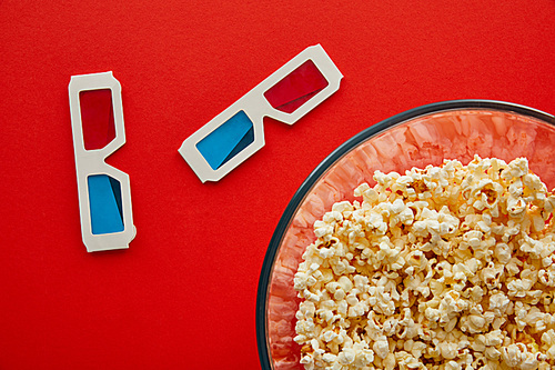top view of delicious popcorn in bowl near 3d glasses isolated on red